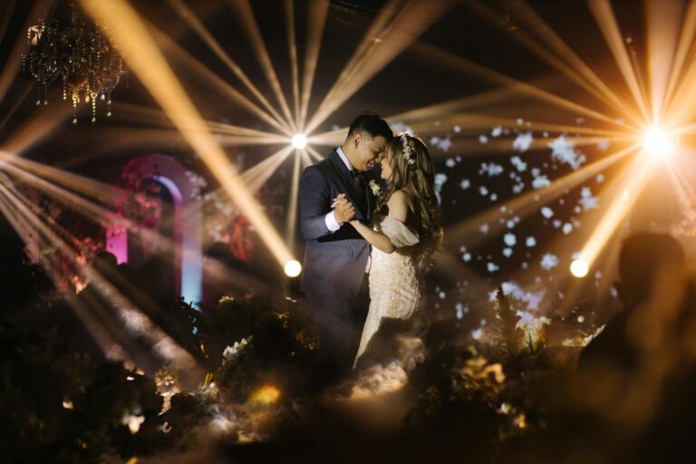 Wedding couple dancing at night with colorful lights and fireworks.
