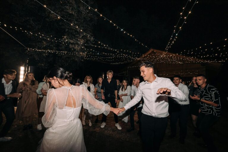 Couple dancing at wedding reception with guests under string lights.