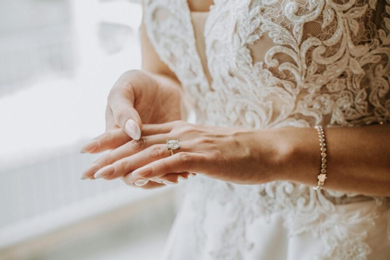 Bridal hands showcasing wedding rings and lace dress details.