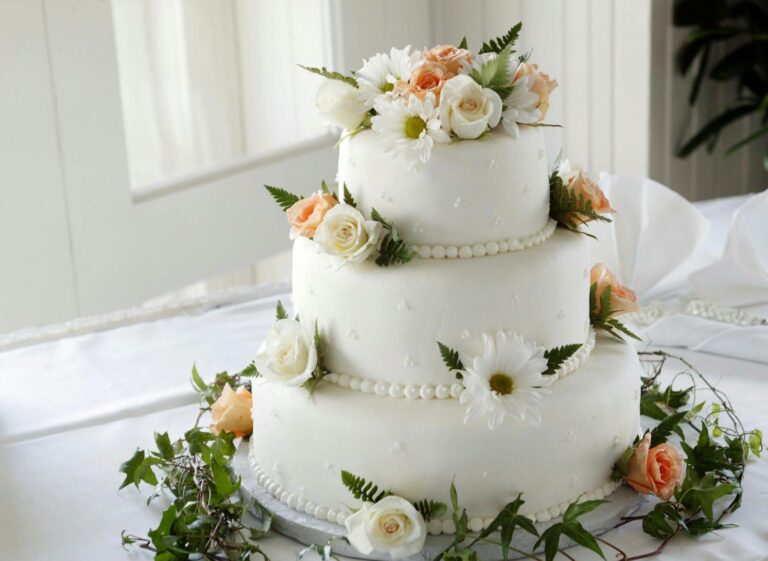 Wedding cake decorated with white and peach roses and greenery.