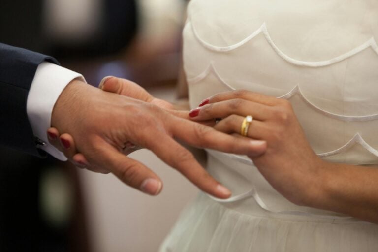 Wedding couple holding hands, close-up of hands with wedding rings.
