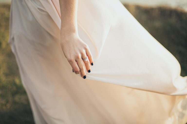Bride's hand holding the flowing wedding dress outdoors.