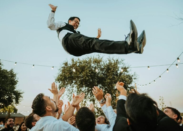 Groom being thrown in the air during wedding celebration outdoors.