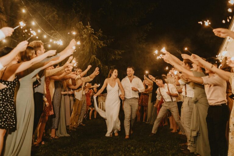 Wedding celebration with sparklers at night, bride and groom walking through guests.