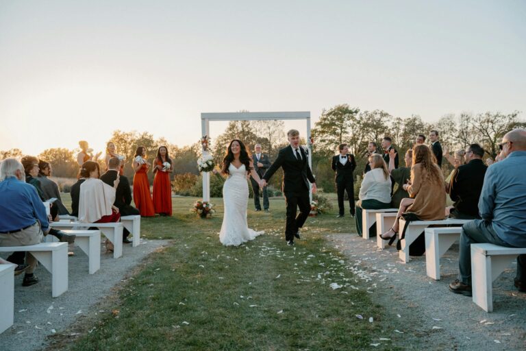 Bride and groom walking hand in hand down the aisle with guests seated on both sides.