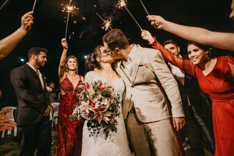 Wedding celebration with sparklers at night, couple sharing a kiss.