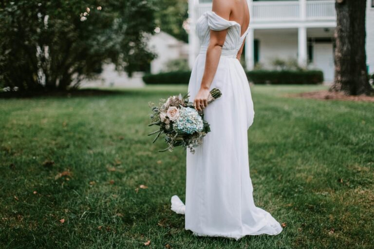 Bride with a bouquet in a white dress standing on grass in a garden.