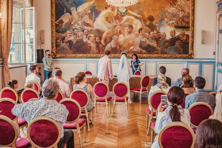 Wedding ceremony in a historic art gallery with guests seated and a couple exchanging vows.
