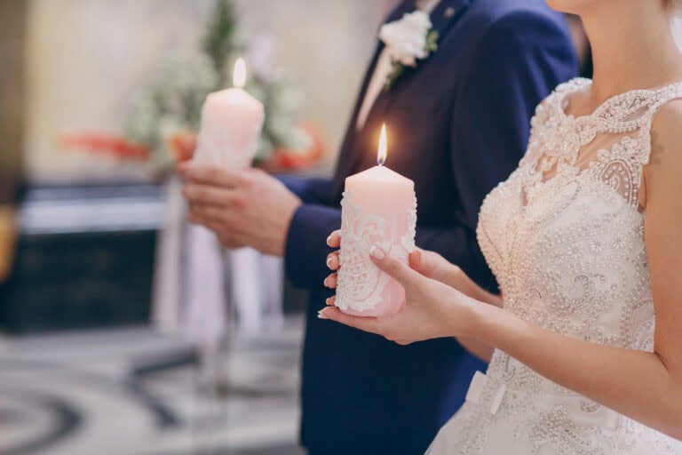 Bride and groom holding lit candles during wedding ceremony.