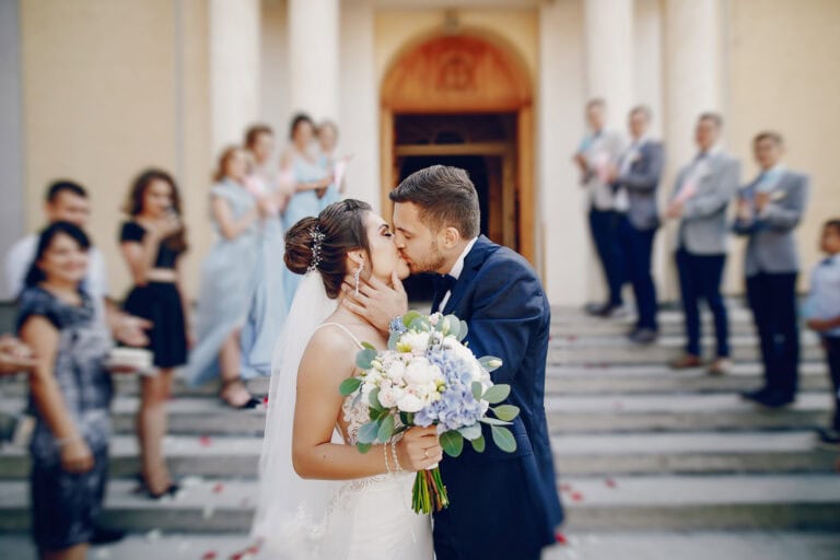 Bride and groom sharing a kiss with wedding guests in the background.