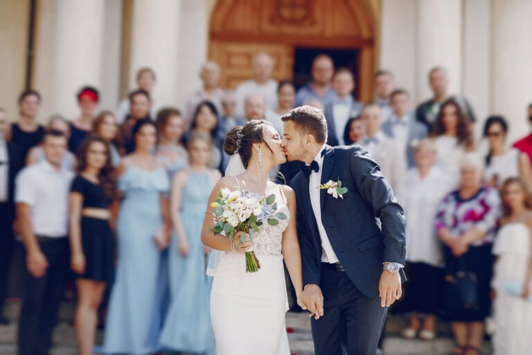 Wedding couple kissing outside church with guests in background.