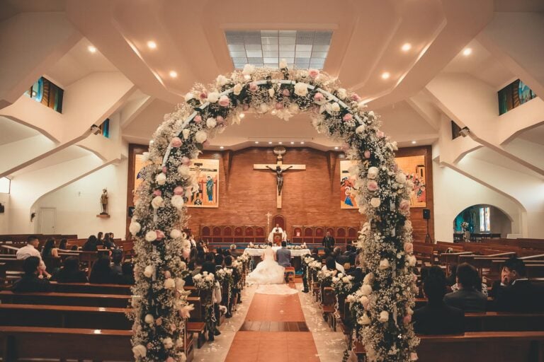 Elegant church wedding with floral arch, altar, and guests seated in wooden pews.