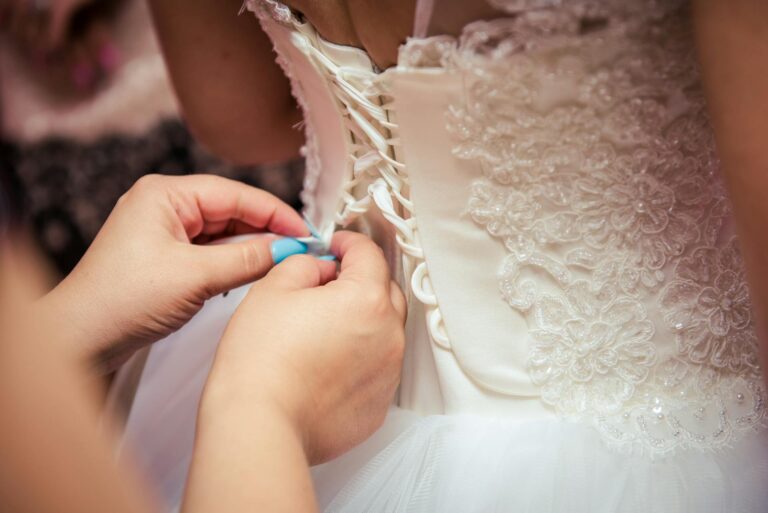Wedding dress being laced up by a bride's hand, showcasing intricate lace details and delicate craft.